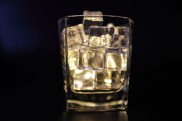 Opaque transparent ice filled drink short glass yellow tungsten light flame smoke fog on black background
