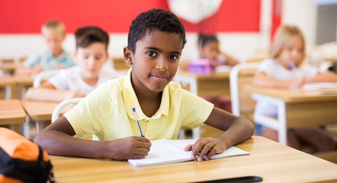 Portrait of smiling african preteen schoolboy sitting on lesson in classroom, looking confidently at camera - Powered by Adobe