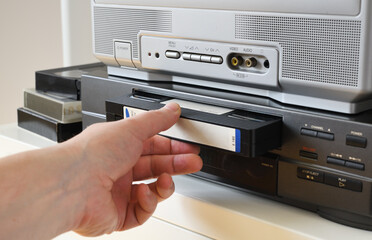 Hand inserting a VHS tape into a video cassette player at home