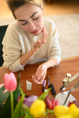 A woman applying a makeup primer to her face in front of a mirror. The makeup products are neatly arranged on the table, highlighting her careful preparation for flawless makeup application.