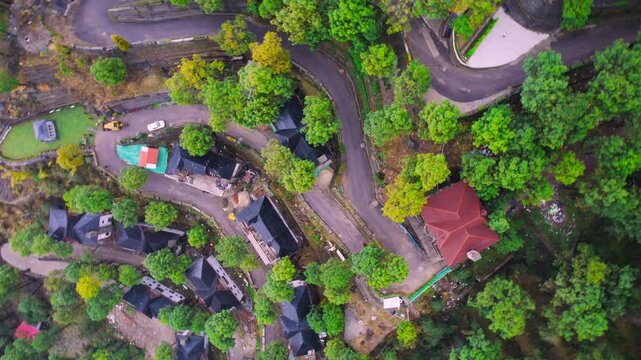 aerial drone shot gaining height and spinning over red roofed houses, cabins built on a winding road on side of Himalaya mountains in Kasauli India showing serenity and natural beauty of hill stations