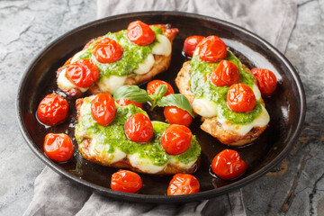 Chicken margherita is made with juicy pan-seared chicken, topped with basil pesto, mozzarella, roasted cherry tomatoes close-up on pan on table. Horizontal