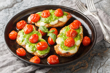 Roasted Margherita chicken breasts topped with melted mozzarella, pesto and cherry tomatoes close-up on pan on table. Horizontal