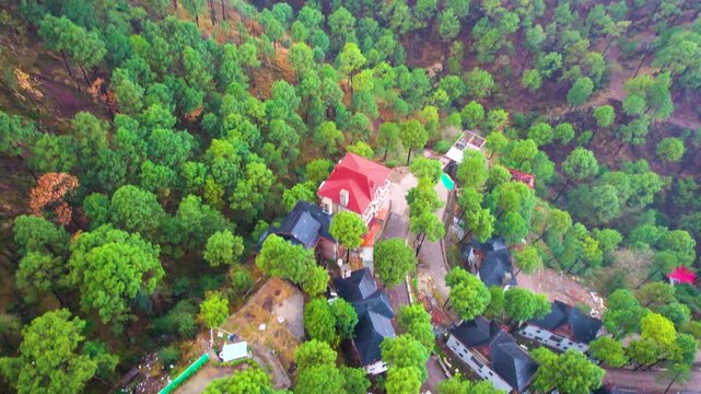 Aerial drone shot panning up reveal from sloping roof opulent home villas to lush green tree jungle and high Himalaya mountains showing India's hills stations