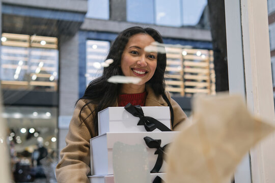 Woman smiling while holding gift boxes outdoors in an urban setting