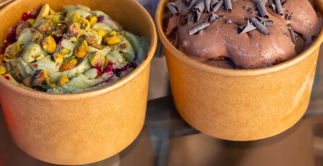 delicious ice cream in cardboard boxes with strawberry,pistachio and chocolate taste. to go dessert for refreshment in sunny summer days, slice of fresh fruits, nuts and grated chocolate as decoration