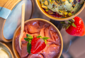 delicious ice cream in cardboard boxes with strawberry,pistachio and chocolate taste. to go dessert for refreshment in sunny summer days, slice of fresh fruits, nuts and grated chocolate as decoration