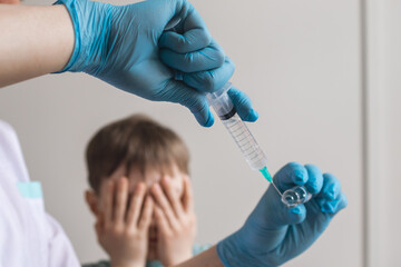 Doctor holding a syringe with injection vaccination. The boy covered his eyes with his hands out of fear. © Mikhail