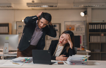 Two overworked and frustrated businesspeople are having a bad time at the office at night,...