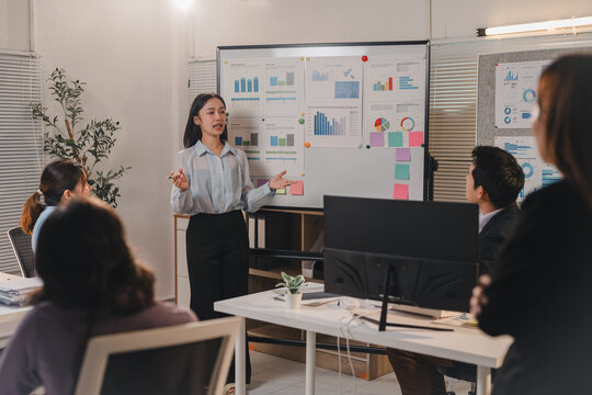 Young businesswoman presenting marketing data on whiteboard to team of colleagues listening attentively during a business meeting in modern office