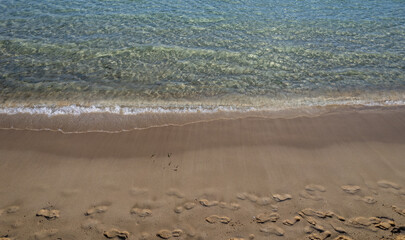 Crystal clear water gently washing sandy beach with footprints