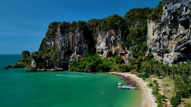 Experience the breathtaking beauty of Thailands coastline featuring dramatic cliffs, vibrant greenery, and traditional boats along a golden sandy beach on a sunny day. Tonsai Beach Krabi