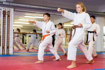 Teenager children wearing karate uniform fighters poses in white kimono during group training in gym © JackF