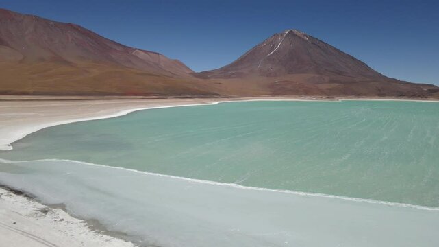 Aerial approach to Laguna Verde in Bolivia with dramatic volcanic mountain rising behind it