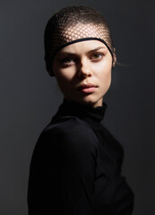 Confident young woman with short hair wearing a black outfit and a fishnet headpiece. Dramatic lighting enhances her strong expression and fierce demeanor.