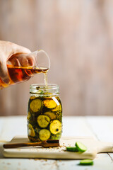 Frau füllig Essig in einem Einmachglas mit Gewürzgurken. Weißer Holztisch.
