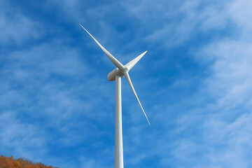 A tall wind turbine stands against a blue sky, harnessing wind energy with its sleek blades.