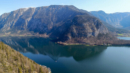 Obraz premium Mountain lake surrounded by forest and rocky cliffs with boat sailing on water surface.