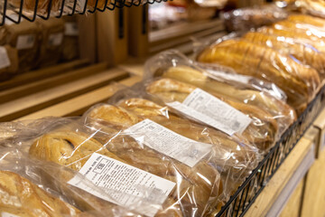 Traditional oval loaves of artisan bread in transparent plastic bags with price labels on wooden shelf in grocery store bakery section, fresh and ready for sale