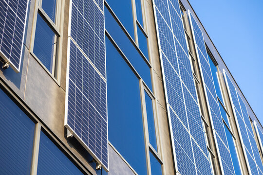 Vertical view of solar panels on modern office building generating renewable energy on sunny day with blue sky and glass reflections in urban architecture - Powered by Adobe