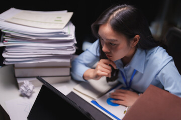 Young asian businesswoman working late in dark office reading reports on her tablet computer with...