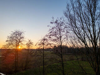 A stunning sunset casts vibrant hues over a serene landscape with silhouetted trees against the...