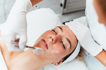 Professional beautician applying glycolic acid peel on face of beautiful young woman. Chemical peeling and beauty treatment concept.