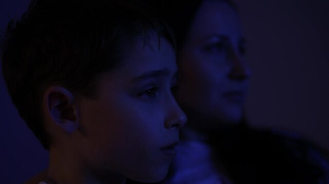 Family watching interactive TV together in a cozy dark room. Child's face illuminated by the blue light of the screen. Family time and entertainment. Family evening watching smart TV apps.