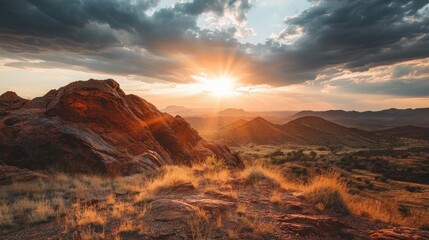 Naklejka premium Majestic Sunset Over Mountain Landscape with Dramatic Clouds and Warm Sunlight Peeking Through Rocky Terrain