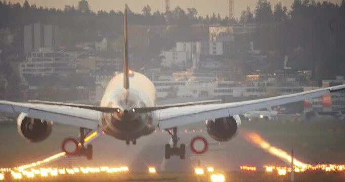 Large, commercial passenger airplane landing on an illuminated airport runway. Ground level, rear of the plane point of view, touchdown and taxi, real time, super-telephoto, early morning light, no pe