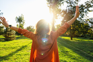 Rear view of woman with raised arms in nature basking in backlit sunshine