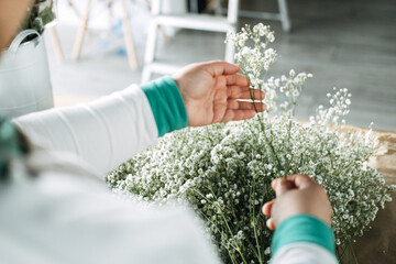 Close-up of a florists hands sorting delicate white baby's breath stems during bouquet preparation...