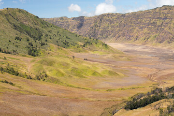 Naklejka premium Wide landscape view of a green valley surrounded by hills under a clear blue sky. A bright and serene natural scene, perfect for travel, nature, and environmental themes.