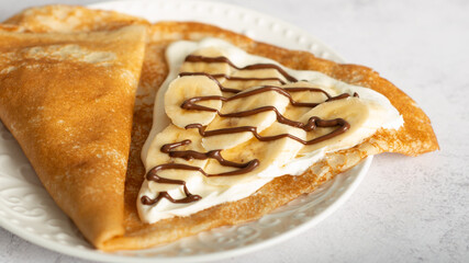 Crepes (thin pancakes, traditional russian dessert blini) with fresh berries, banana slices, melted chocolate and green mint. Maslenitsa concept.