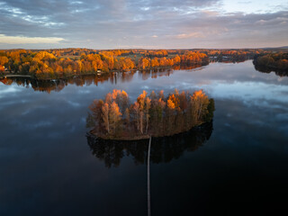 Calm water of the Hejtman pond in Southern Bohemia. Idyllic island captured during colorful autumnal season.