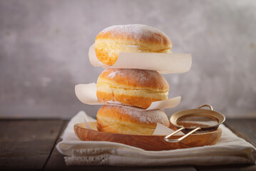 Bomboloni, Italian donuts with cream dusted with powdered sugar, served on a rustic wooden table.