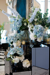 Wedding decoration. An elegant floral arrangement with blue and white hydrangeas in dark vases on mirrored pedestals creates a refined and modern atmosphere for the celebration.