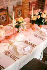 Personalized invitation lies on a knotted napkin on a plate on a festive table near a bouquet of flowers