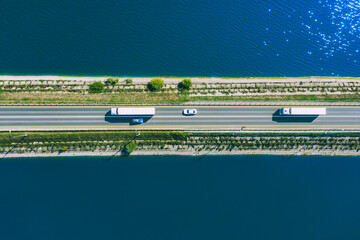 Aerial drone view of freight transporter semi-trucks and cars driving on bridge road over blue sea