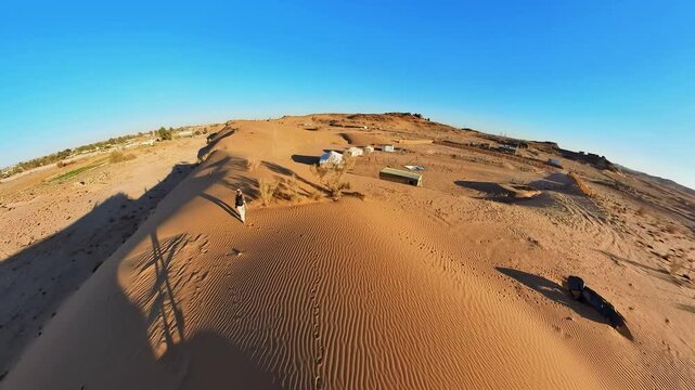 woman photographer, girl walks across the undulating sand dunes near a desert camp in Tabuk, Saudi Arabia, their camera capturing the vast expanse of the desert under a vibrant blue sky