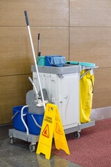 Cleaning cart with mop, bucket, and cloths stands in a hallway alongside a 