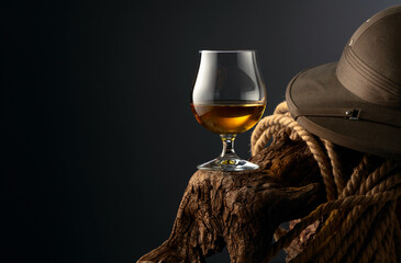 Snifter of brandy, cork tropical colonial helmet and rope on a old wooden snag.