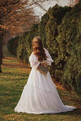 Back view of woman in lace dress with book, walking down quiet path under trees, wrapped in...