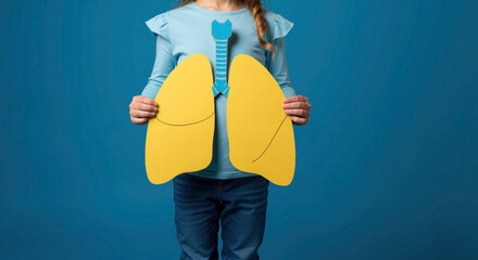 Child holding paper lungs and trachea model against blue background. Young girl demonstrating human respiratory system. World Lung Day, asthma awareness, children's health programs. Horizontal banner