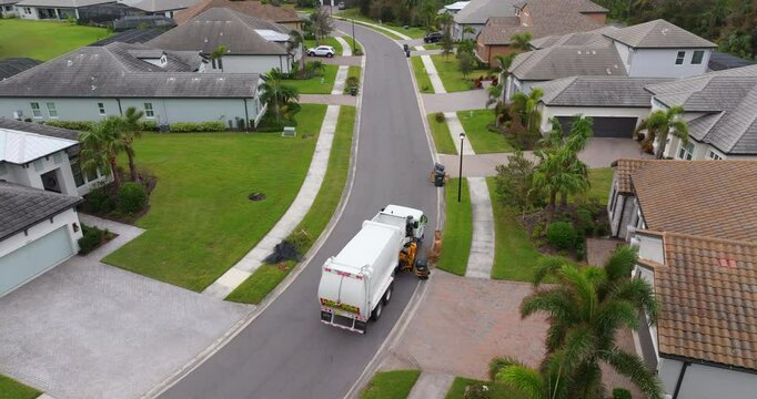 Garbage truck picking up trash bins on suburban street side.