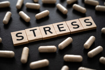 Word stress composed with wooden alphabet on a black background, and around medicinal tablets. Care of anxiety.