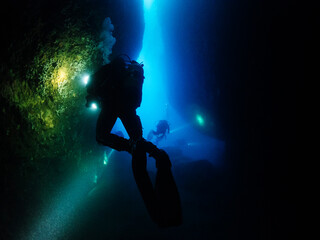 group of scuba divers diving inside a marine cave that they illuminate with their flashlights, concept of active leisure lifestyle and underwater adventure