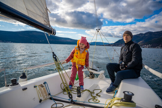 Father instructing daughter on sailing a yacht during training in the Kotor Bay, Montenegro, highlighting family bonding, adventure, and nautical sport.