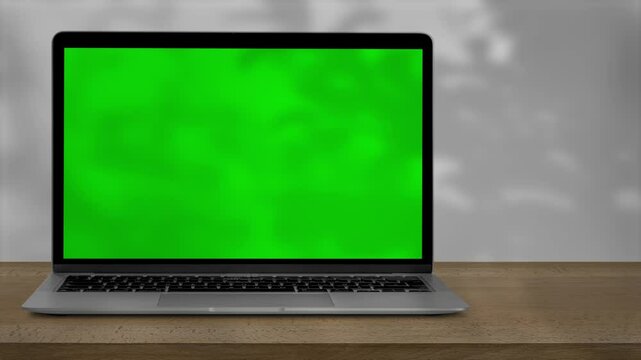a laptop with green screen outdoors, trees swaying in the background.