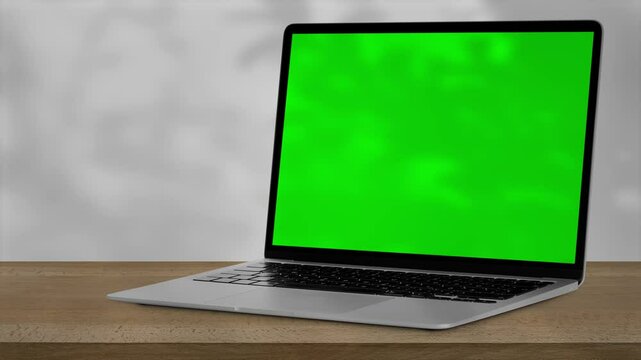 a laptop with green screen outdoors, trees swaying in the background.